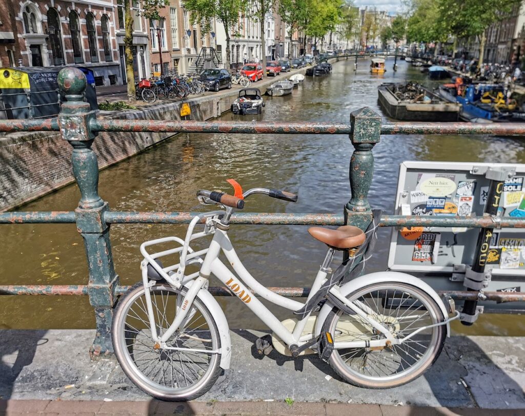 An abandoned Amsterdam bike locked to a bridge railing on a canal